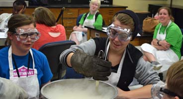 Blind teens smile in a classroom as they stir dry ice to make ice cream.